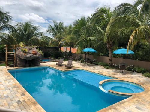 a pool with chairs and umbrellas and palm trees at Pousada Tia Nena in Olímpia