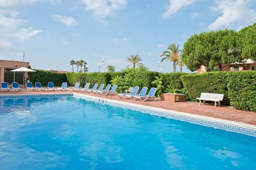 a large swimming pool with chairs and trees and bushes at Pierre & Vacances Comarruga in Comarruga