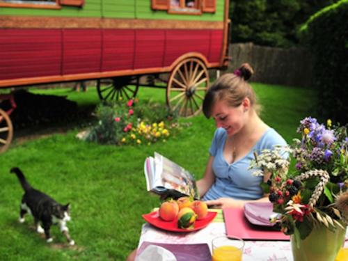 a woman sitting at a table with a cat looking at a book at Les Roulottes de Troussures in Troussures