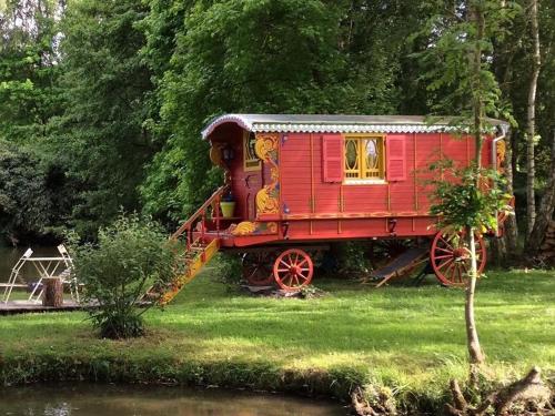 a red train sitting in the grass next to a river at Les Roulottes de Troussures in Troussures