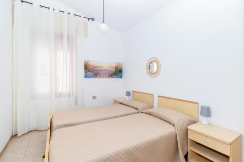 a white bedroom with two beds and a window at Casa Spiaggia Molo 2 in Isola Rossa