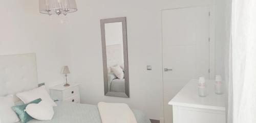 ein weißes Zimmer mit einem Bett und einem Spiegel in der Unterkunft Piso 100 metros del Centro del Pueblo 6 kilómetros de la PLAYA La BARROSa in Chiclana de la Frontera