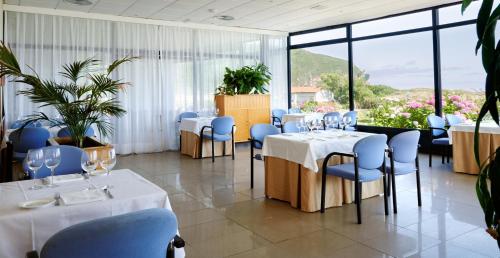 a restaurant with white tables and blue chairs and windows at Hotel Juan de la Cosa in Santoña