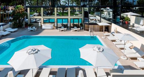 a swimming pool with white umbrellas and chairs at Hotel Sporting in Rimini