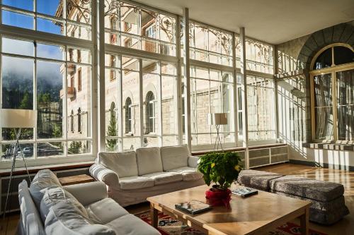 a living room with couches and a table and windows at Maloja Palace Residence Engadin-St Moritz CO2-Neutral in Maloja