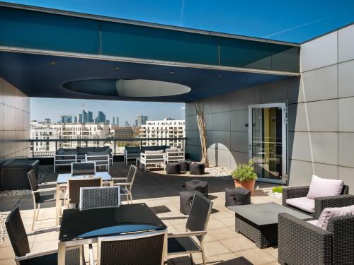 eine Dachterrasse mit Stühlen und Tischen und Stadtblick in der Unterkunft Plaza Hotel & Living Frankfurt in Frankfurt am Main