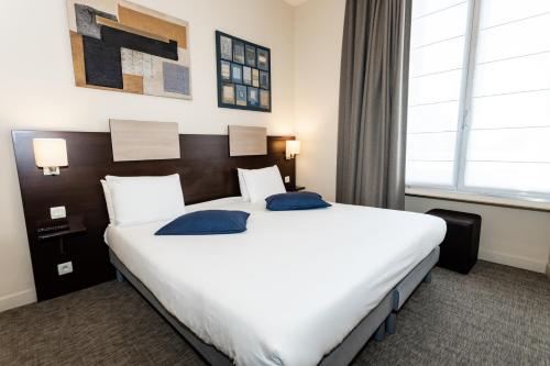 a hotel room with a large white bed with blue pillows at Hôtel de Champagne in Angers