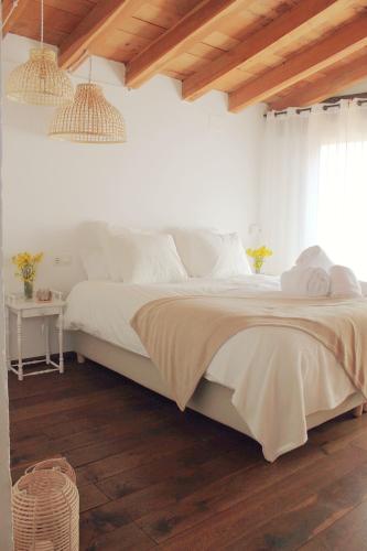 a bedroom with a bed with white sheets and wooden floors at El Niu Casa Rural in Montagut