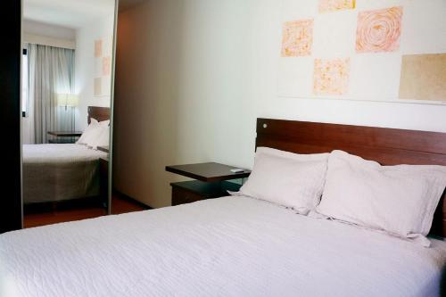 Schlafzimmer mit einem Bett mit weißer Bettwäsche und einem Spiegel in der Unterkunft Rio Sunset Arpoador! in Rio de Janeiro