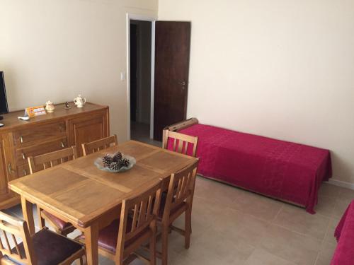 Miramar - Depto 2 ambientes في ميرامار: غرفة طعام مع طاولة وسرير احمر