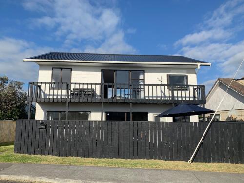 a white house with a black fence and an umbrella at Sand Dunes Retreat in Otaki Beach