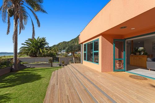a house with a wooden deck next to the ocean at The Lights House - Beachfront Ohope Holiday Home in Ohope Beach