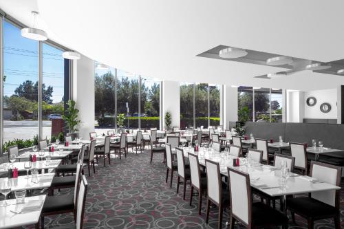 a dining room with white tables and chairs and windows at Mantra Melbourne Airport in Melbourne
