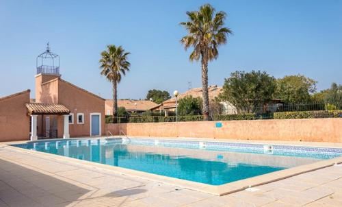une grande piscine avec des palmiers en arrière-plan dans l'établissement Maison vacances résidence privée Piscine Loupian-Mèze, à Loupian