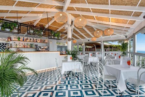 a restaurant with white tables and chairs on a tile floor at Gocce Di Capri Resort in Massa Lubrense