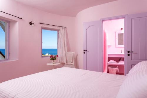 a white bedroom with a white bed and a window at Windmill Villas in Imerovigli