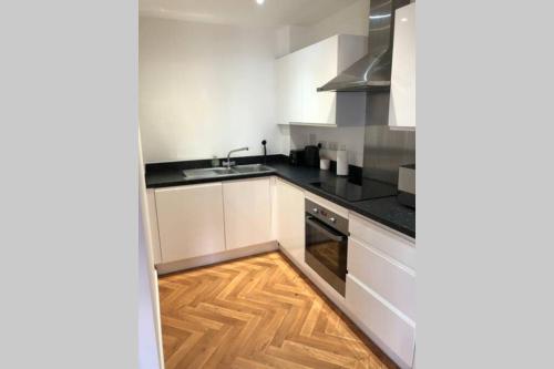 a kitchen with white cabinets and a wooden floor at 2 Double beds OR 4 Singles, 2 Bathrooms, FREE PARKING, Smart TV's, Close to Gunwharf Quays, Beach & Historic Dockyard in Portsmouth