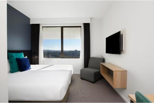 ein Hotelzimmer mit einem Bett, einem TV und einem Stuhl in der Unterkunft Mantra MacArthur Hotel in Canberra