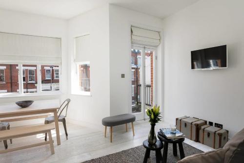 a white living room with a table and a chair at GuestReady - West Kensington Home wBalcony in London