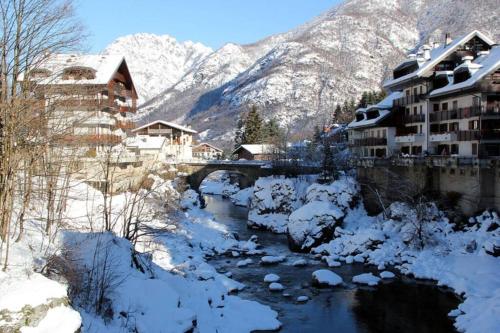 a snow covered village with a river and snowy mountains at Baita Coccola nel Bosco Sport Natura Relax in Scopello