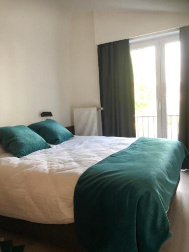a bedroom with a bed with green pillows and a window at duunn koksijde in Koksijde