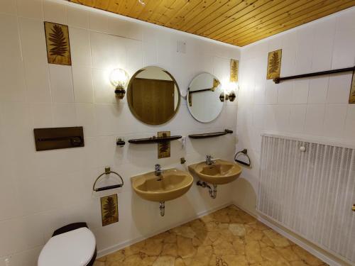 a bathroom with two sinks and a toilet and mirrors at Pension Berg&Bleibe Wertach in Wertach