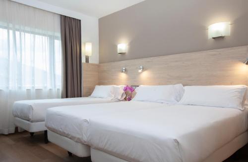 two beds in a hotel room with white sheets at Hotel Puerta de Bilbao in Barakaldo