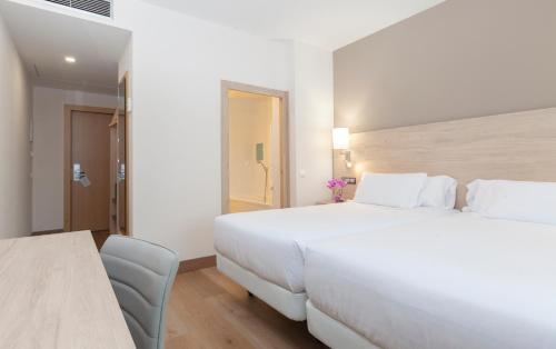 a white bedroom with a large bed and a table at Hotel Puerta de Bilbao in Barakaldo