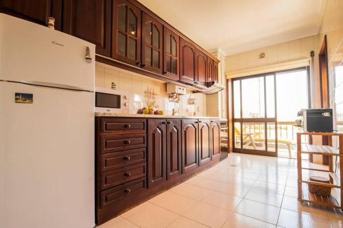 a kitchen with a white refrigerator and wooden cabinets at CASA DOS FARÓIS GARAGEM GRATUITO PRAIA DA BARRA in Gafanha da Nazaré