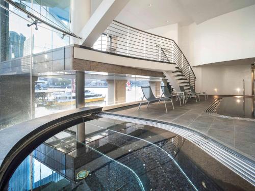 a swimming pool in a building with a staircase and chairs at Pullman Quay Grand Sydney Harbour in Sydney
