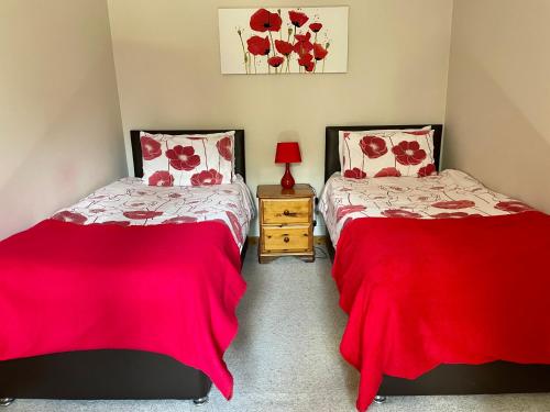 twee bedden in een kamer met rode lakens bij Derrybrook Cottage, Twin or Superking, Seven Springs Cottages in Cheltenham