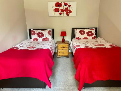 2 Betten in einem Zimmer mit roter Bettwäsche in der Unterkunft Derrybrook Cottage, Twin or Superking, Seven Springs Cottages in Cheltenham