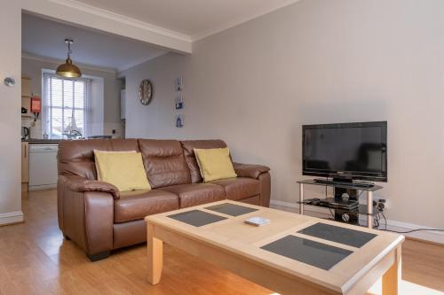 a living room with a brown couch and a tv at Stonehaven ground floor home with a spectacular harbour view. in Stonehaven