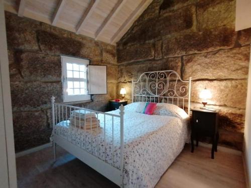 ein Schlafzimmer mit einem weißen Bett in einer Steinmauer in der Unterkunft Casa antiga de pedra com piscina e vista rio in Amarante