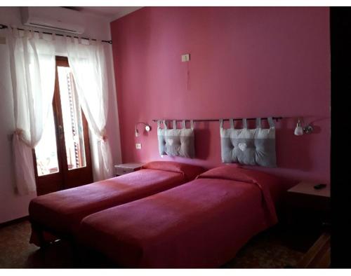- 2 lits dans une chambre avec des murs roses et une fenêtre dans l'établissement Hotel Torre, à Vulcano