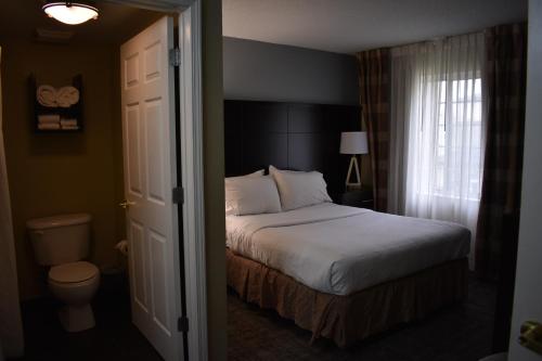 a bedroom with a bed and a toilet and a window at Staybridge Suites Cranbury - South Brunswick by IHG in Cranbury