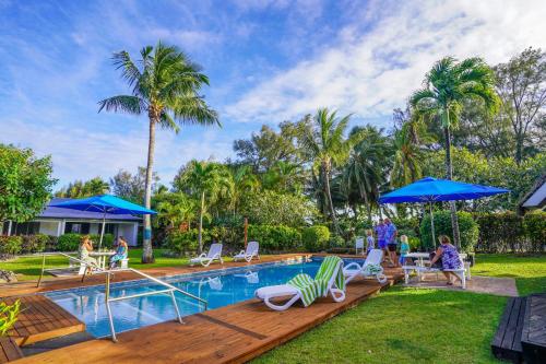 a pool with chairs and umbrellas in a yard at The Black Pearl Beachside Apartments in Rarotonga