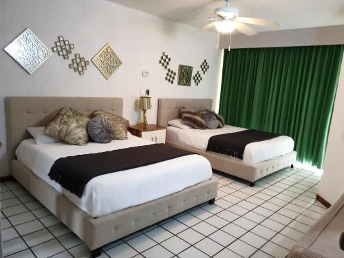- 2 lits dans une chambre avec des rideaux verts dans l'établissement Colibri Paradise Puerto Aventuras, à Puerto Aventuras