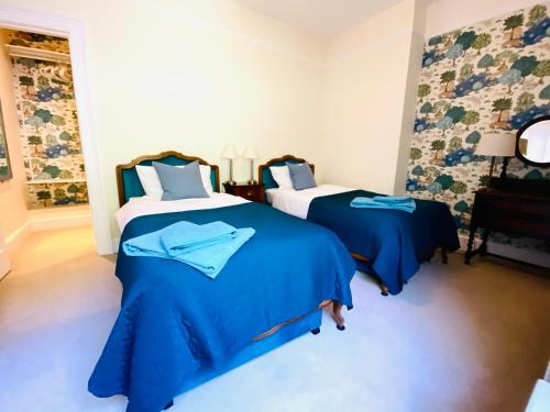 a bedroom with two beds with blue sheets and a window at Clarendon View, Historic Apartment with Sea Views in Ventnor