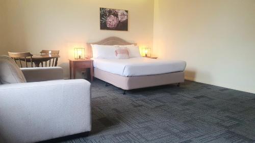 a bedroom with a bed and a chair and a table at Hotel Cavalier in Wantirna South
