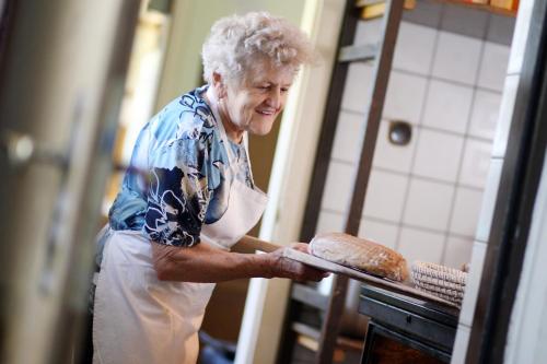 an older woman putting a loaf of bread into an oven at Perbersdorfer Heuriger in Neuhofen an der Ybbs