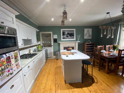 a kitchen with white cabinets and a dining room with a table at Chemist's House in Cullen