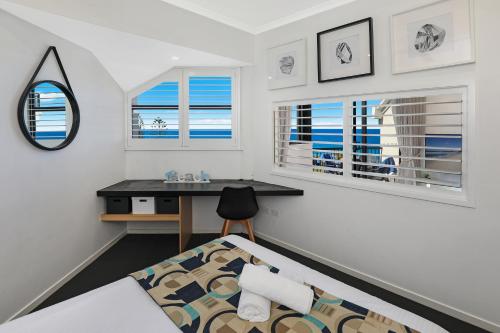 a bedroom with a bed and a desk and windows at Ocean Boulevard in Alexandra Headland