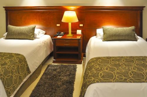 a hotel room with two beds and a lamp on a table at Gran Amérian Carlos V in Termas de Río Hondo