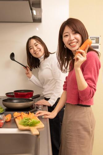 two women standing in a kitchen holding a carrot at ゲストハウス岐阜羽島心音 Guest House Gifuhashima COCONE in Hashima