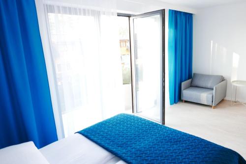 a bedroom with blue curtains and a bed and a chair at Apartamenty Marco Polo in Dziwnówek