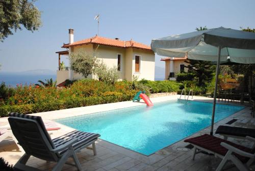 a swimming pool with chairs and an umbrella and a house at Villa Thea in Ancient Epidauros