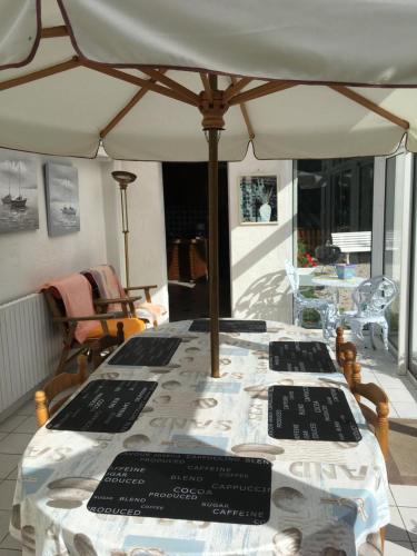 une table avec des panneaux noirs et un parapluie dans l'établissement Maison Proche de Barfleur accolée à un commerce, à Anneville-en-Saire