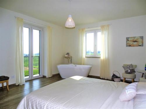 a bedroom with a white bed and a tub and windows at Al Tirabusòn Country House in Nizza Monferrato