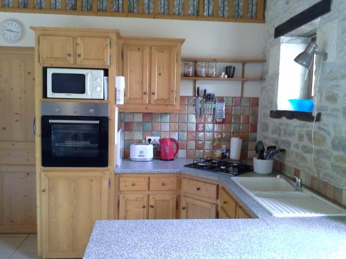 a kitchen with wooden cabinets and a microwave and a sink at La Vieille Gorce Gîtes in the Vienne in Asnois